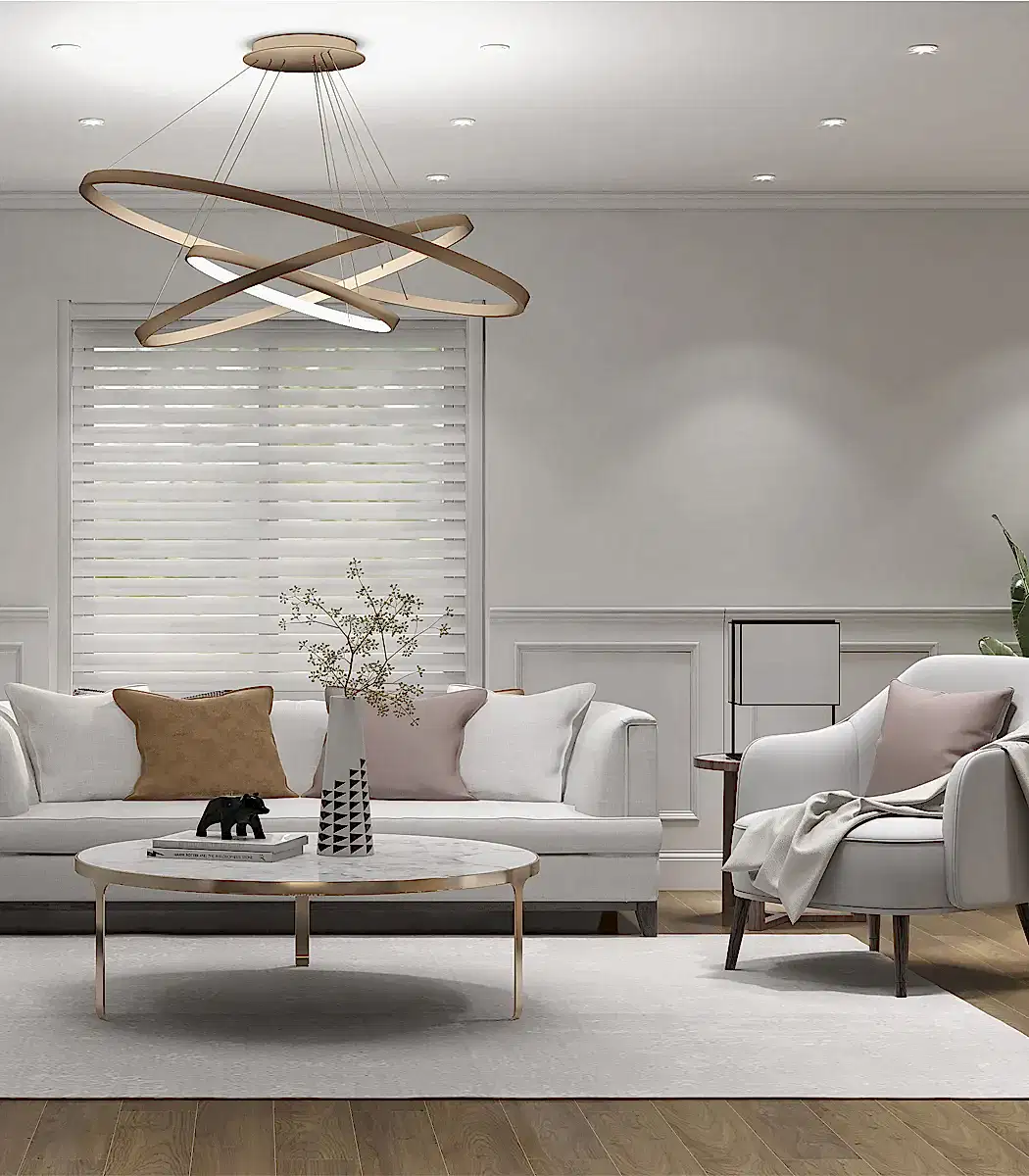 Modern oturma odasında Premium gri kanepe, beyaz koltuk, yuvarlak sehpa ve geometrik avize bulunmaktadır. Dekorda yastıklar, bir bitki ve soyut öğeler yer almaktadır. Perdeli pencere ışığı, her ayrıntıya iç mimar dokunuşu katarak şık villa havasını güçlendirir.