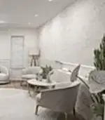 İç mimarın tarzıyla tasarlanmış, Premium açık gri sandalyeler, yuvarlak masa, ayaklı lamba ve dekoratif bitkilerle donatılmış modern bir oturma odası. Mermer desenli duvarlar, panjurlu küçük pencereyi tamamlayarak, özel bir villanın zarafetini yansıtıyor.