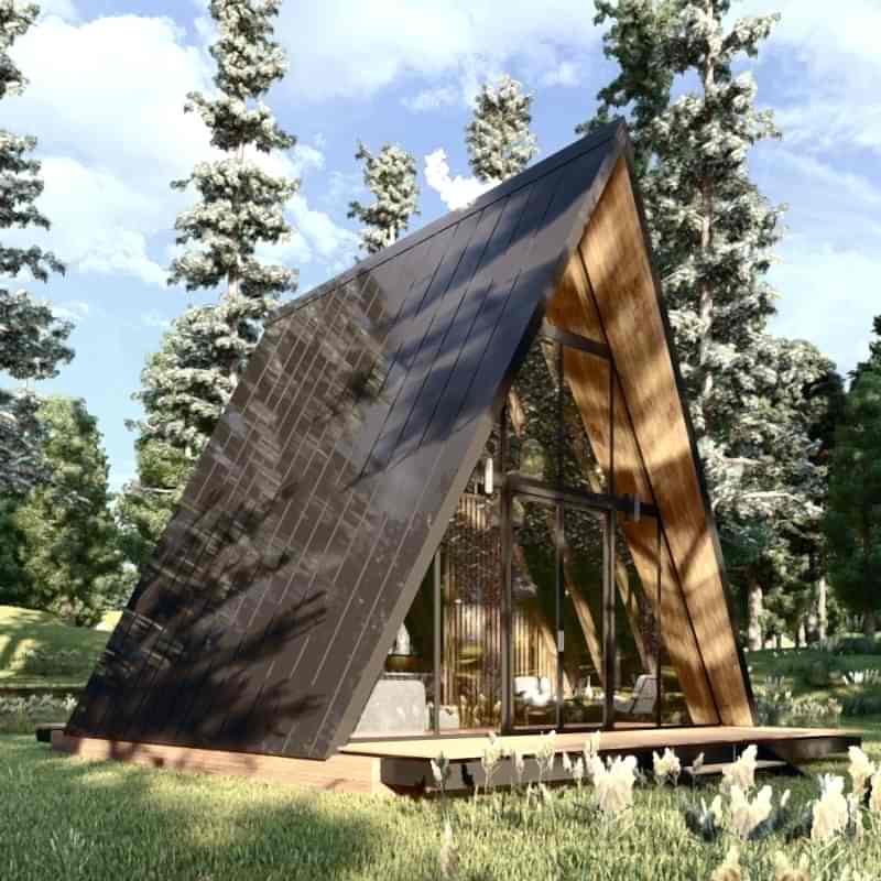 Kısmen bulutlu bir gökyüzünün altında, çimenli bir alanda, ağaçların arasında konumlanmış, şık bir iç mimar villası gibi tasarlanmış, bir tarafı koyu renkli güneş panelleriyle kaplı modern bir A tipi kabin.